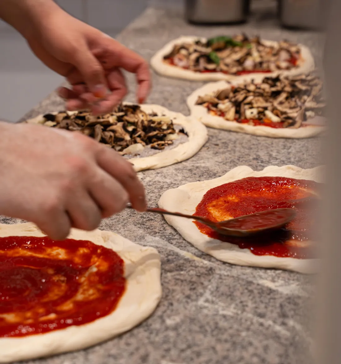 La sauce tomate étalée à la cuillère sur une rangée de pizzas